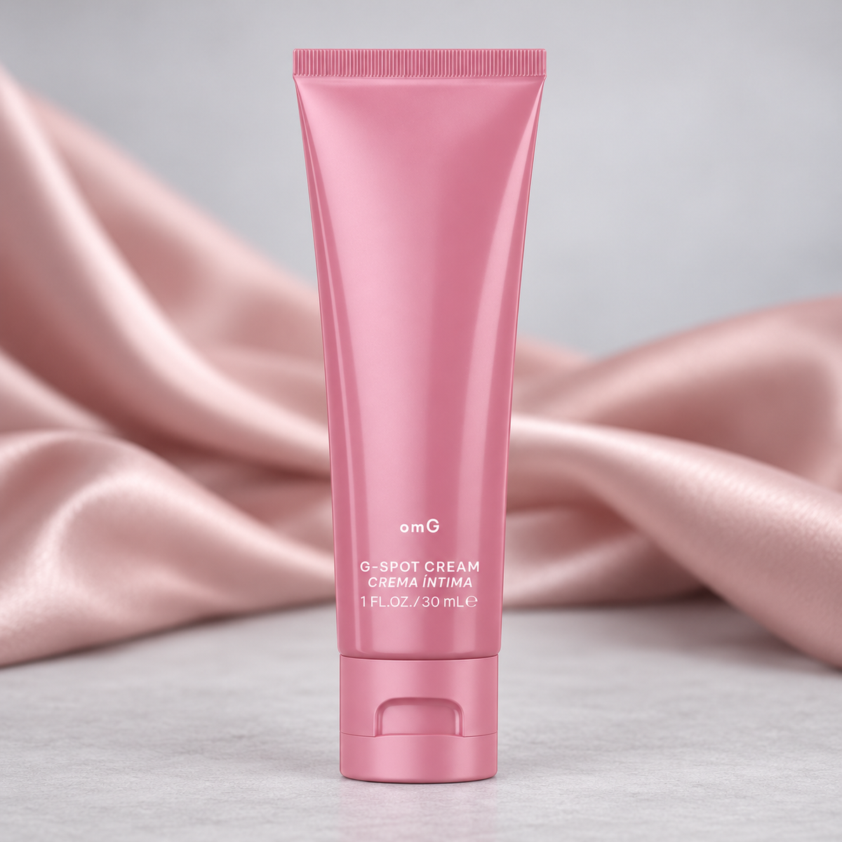 omG G-Spot Enhancement Cream pink tube showcased with blush satin on a grey surface