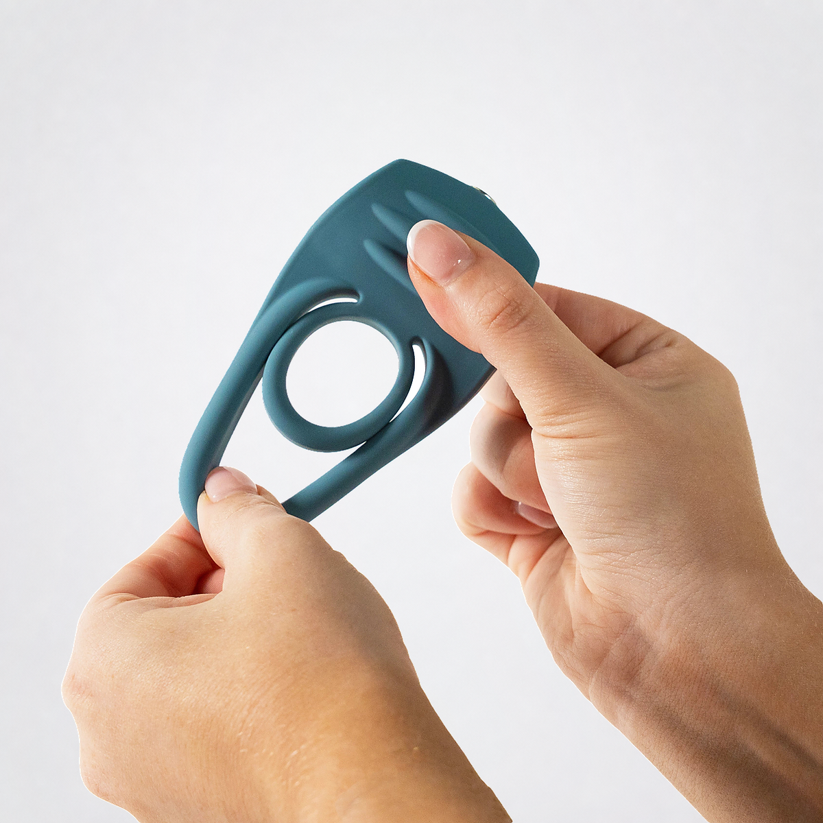 Hands stretching the flexible teal Ring My Bell double C-ring on a neutral grey background