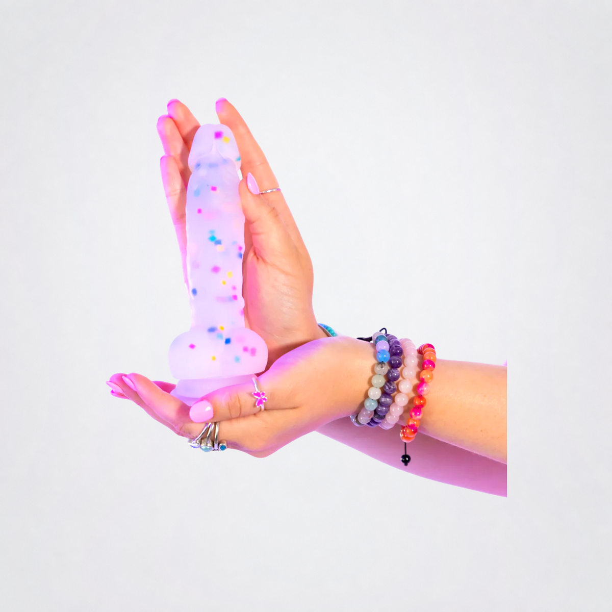 Cock-A-Palooza confetti silicone dildo held between two hands on a neutral gray background
