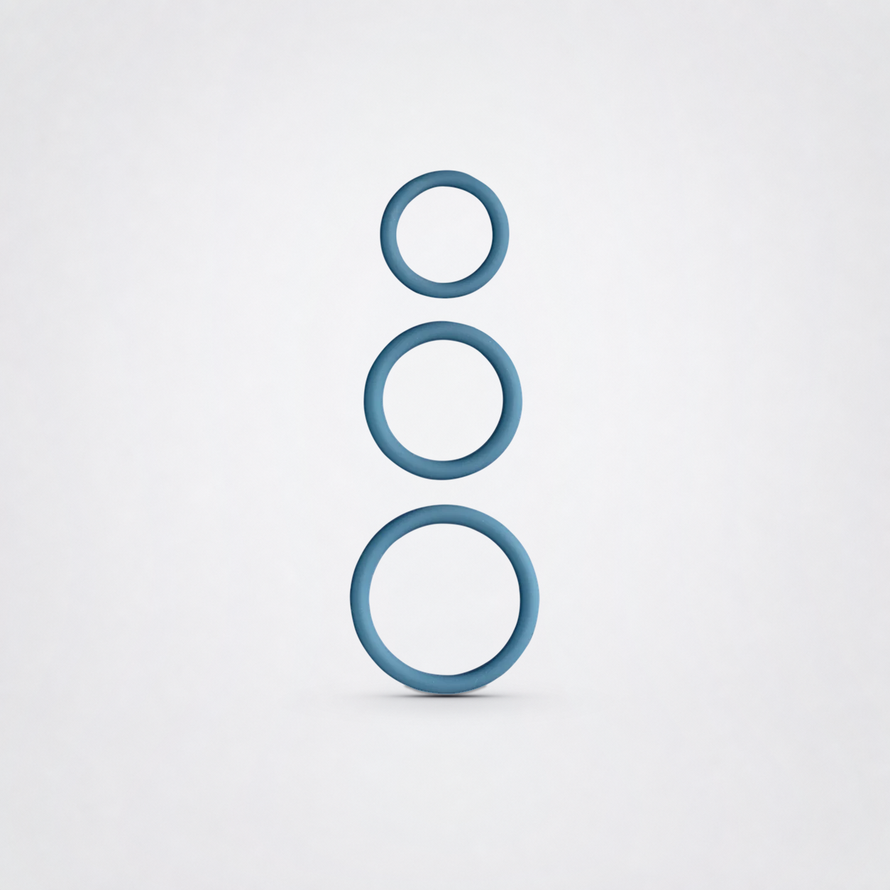 Three blue silicone penis rings in graduated sizes on a neutral grey studio background