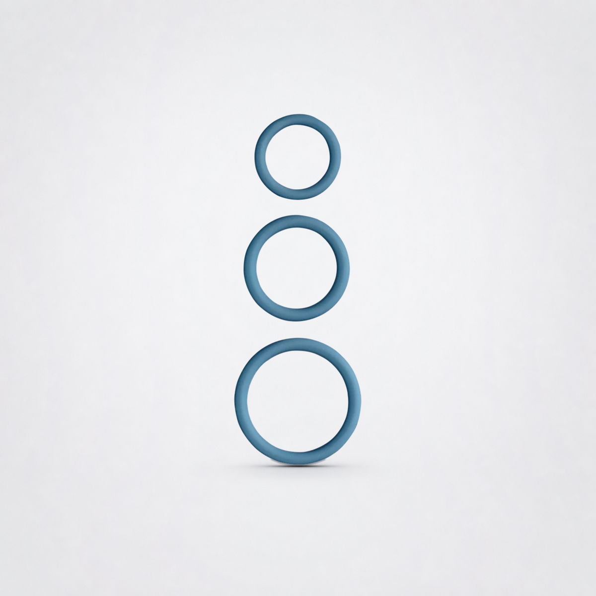 Three blue silicone penis rings in graduated sizes on a neutral grey studio background
